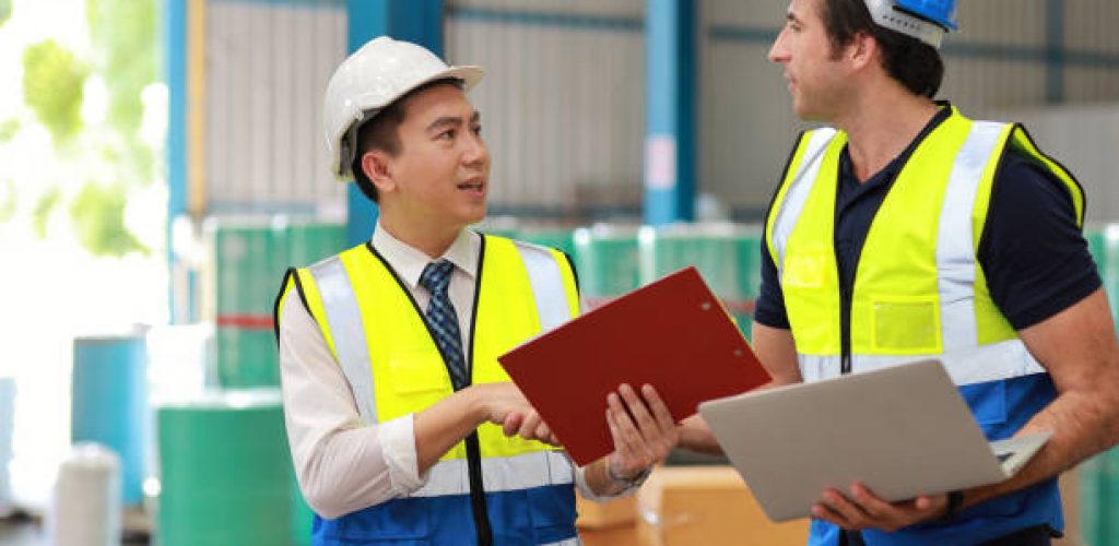 Two technician engineer man in protective uniform with hardhat standing and shaking hands celebrate successful together or completed deal commitment at industry warehouse manufacturing factory